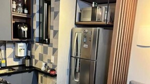 Une cuisine compacte équipée d’un réfrigérateur encastré, d’une machine à café et d’une étagère où sont disposés des objets décoratifs.