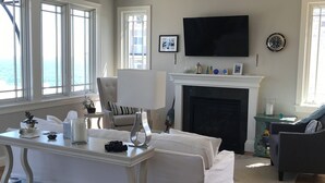 Una sala de estar con chimenea, televisor montado en la pared y un ventanal con vistas al exterior.