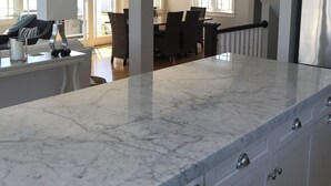Una cocina moderna con encimeras de mármol, armarios blancos e iluminación colgante.