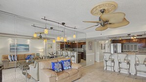 A spacious living room with a large sofa, a dining area, and a kitchen with bar stools. - New Listing! Third Floor Condo Close to Beach With Pool Views. (Saint Augustine)