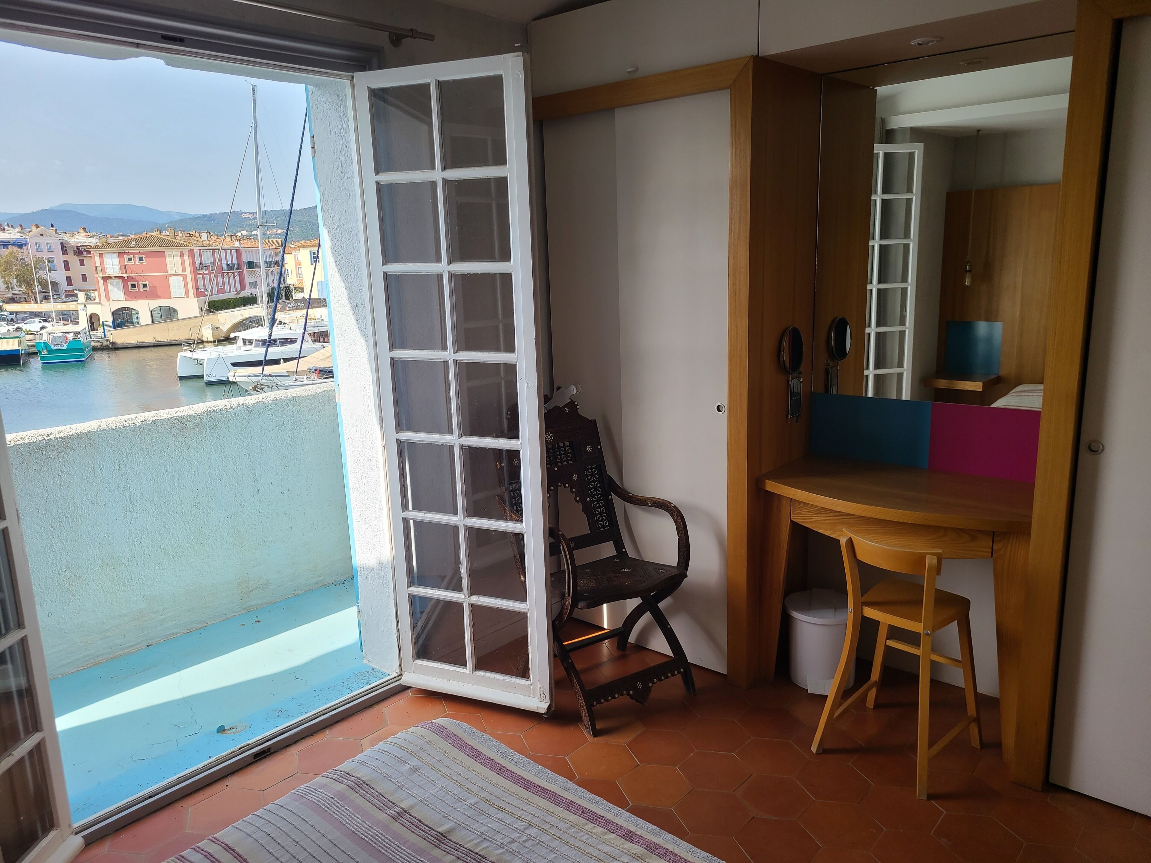 A balcony with a view of boats and buildings, a wooden chair, a small table, and a mirror.