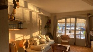 Un salon chaleureux avec un canapé, un fauteuil en osier et une grande fenêtre donnant sur le port.