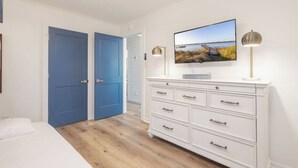 Un dormitorio con una cama, un aparador blanco, un televisor y dos puertas azules.