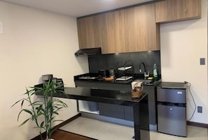 A modern kitchen with wooden cabinets, a black countertop, a built-in stove, a refrigerator, and a potted plant.