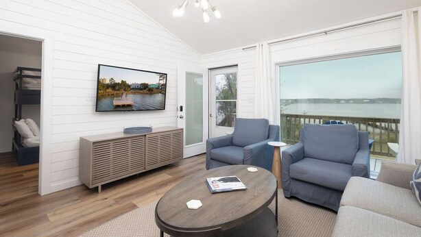 Una sala de estar moderna con un televisor grande, asientos cómodos y vista al agua.