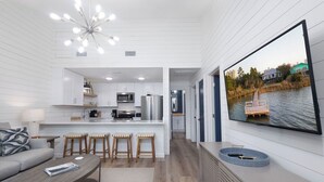 Un interior moderno con cocina, comedor y una gran pantalla de televisión que muestra una vista panorámica.