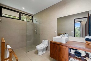 Ein modernes Badezimmer mit einer Glaskabine zur Dusche, einer weißen Toilette und einem Holzwaschtisch.