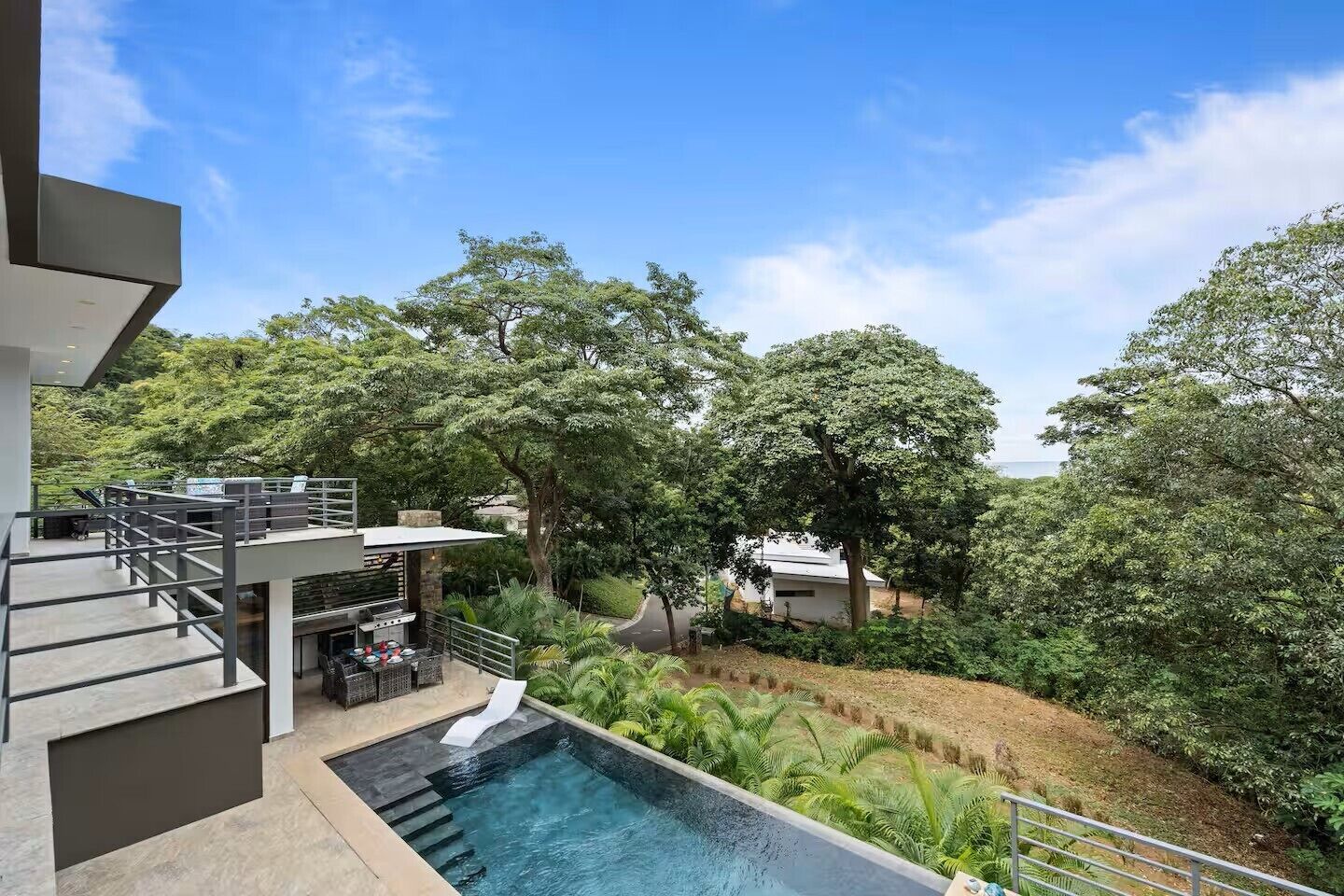 A modern outdoor pool area with a clear view of the surrounding lush greenery and a multi-level structure with outdoor seating.