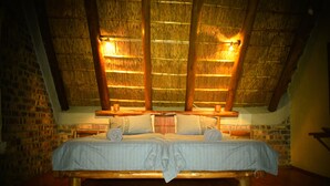 Una habitación con una cama de madera, paredes de ladrillo y un techo de paja.