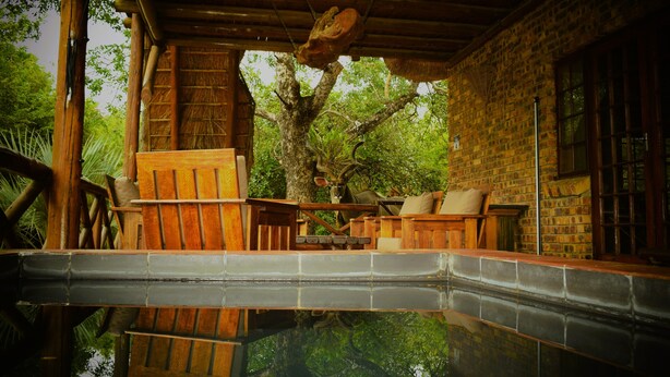 Una terraza de madera con piscina, un muro de piedra y un árbol.