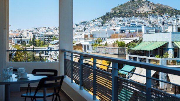 A balcony with a table and chairs, overlooking a cityscape with buildings and a hill. - Urbanised Pangrati 2 bedroom Luxury (Athina)
