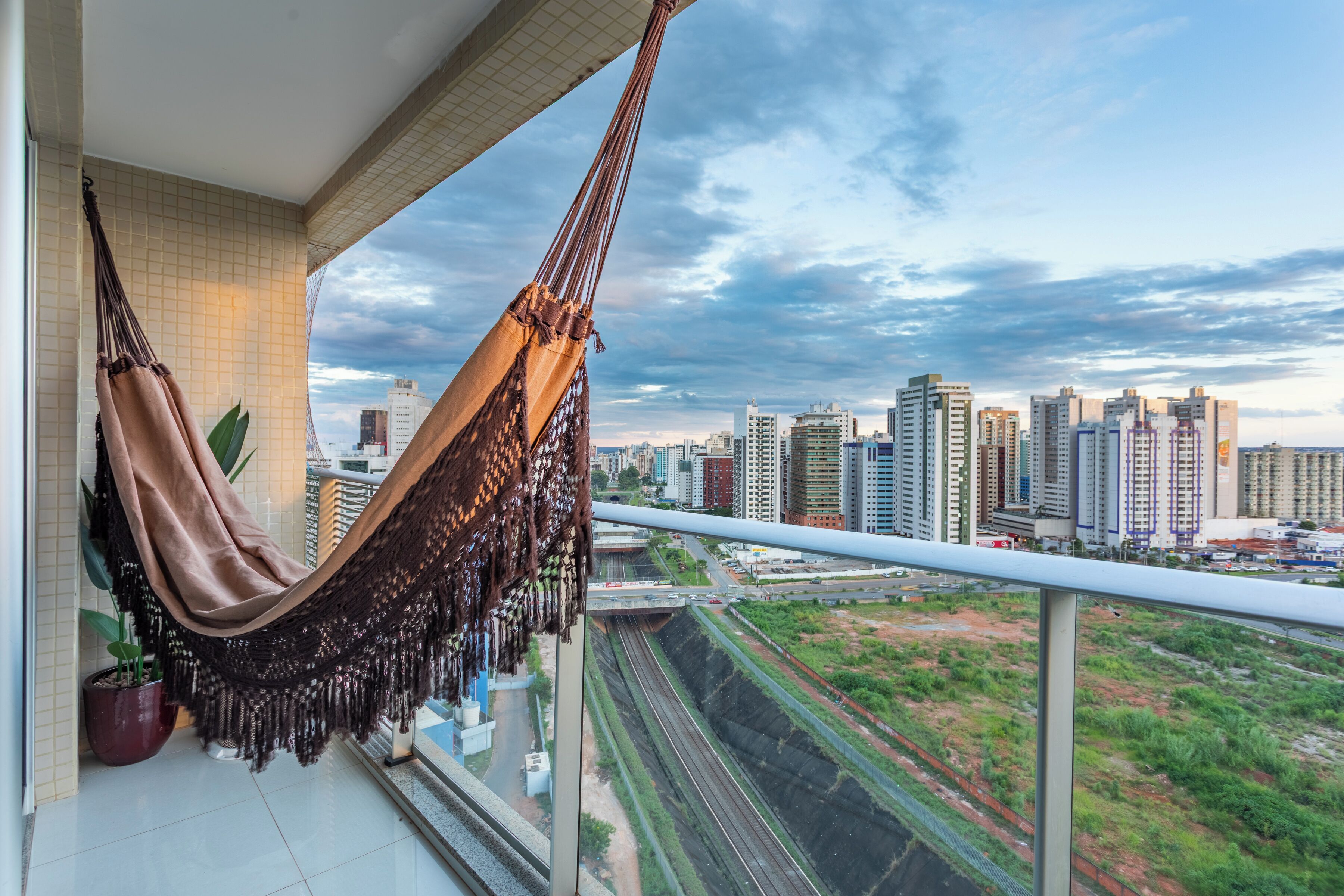 Uma rede numa varanda com vista para uma paisagem urbana, com edifícios altos e uma linha férrea.