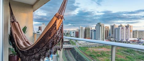 Una hamaca en un balcón con vistas a un paisaje urbano con edificios altos y una vía de tren.