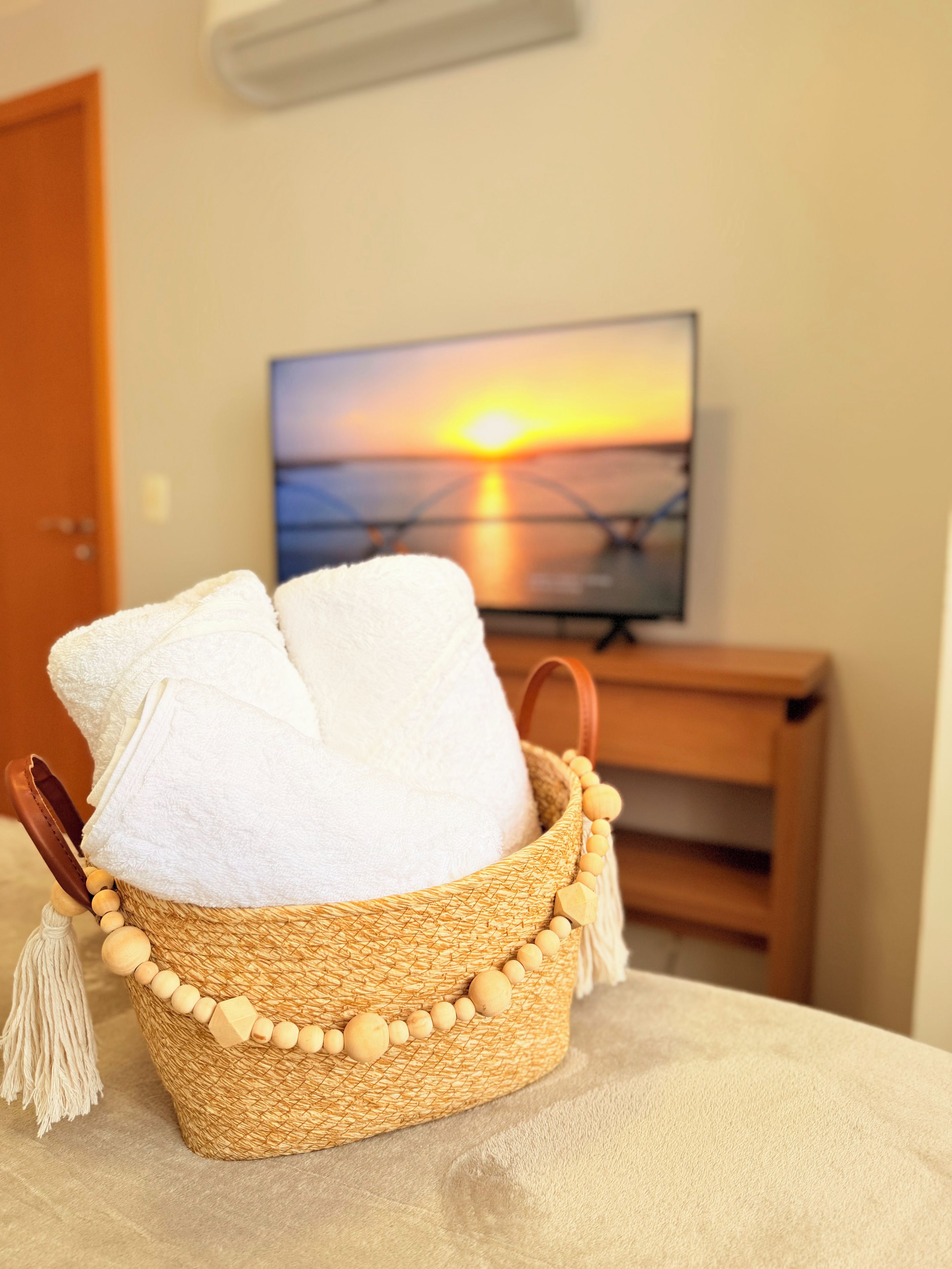 Een gevlochten mand met een handdoek, geplaatst op een bed met uitzicht op een zonsondergang aan de muur.