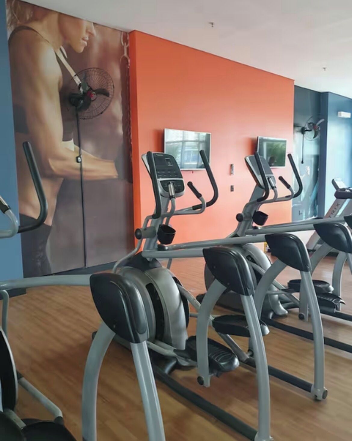 A gym with treadmills, a wall-mounted TV, and a large poster of a woman exercising.