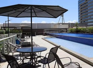 An outdoor pool area with a seating arrangement and a large umbrella. - Lightness and Comfort: DFPlaza Shopping Águas Claras (Águas Claras)