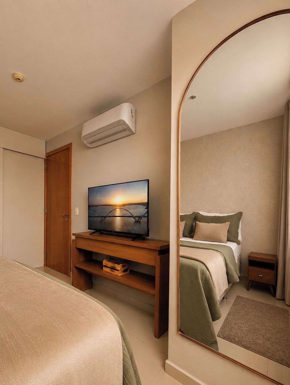 Ein Hotelzimmer mit einem Bett, einem Fernseher auf einem Holzboden, einem Spiegel und einer Klimaanlage an der Wand.