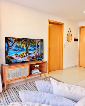 A living room with a flat-screen TV, wooden furniture, a door, and a wall-mounted telephone. - Lightness and Comfort: DFPlaza Shopping Águas Claras (Águas Claras)