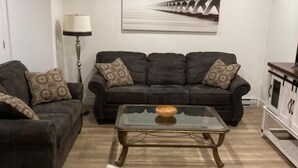 Een woonkamer met een donkerbruine zithoek, een glazen salontafel en een witte fauteuil.