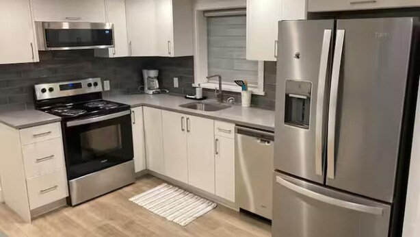 Een moderne keuken met roestvrijstalen apparatuur, witte kasten en een betegelde spatwand.