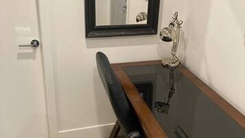 Een kamer met een witte deur, een zwarte stoel, een houten bureau en een spiegel aan de muur.