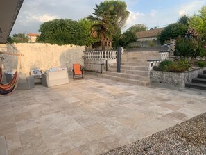 Eine Terrasse mit Steinboden, einer Hängematte, einem Stuhl und einem kleinen Tisch.
