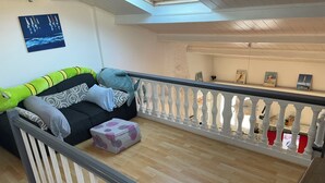 Ein Balkon mit Holzboden, weißer Reling und einer Couch mit verschiedenen Kissen.