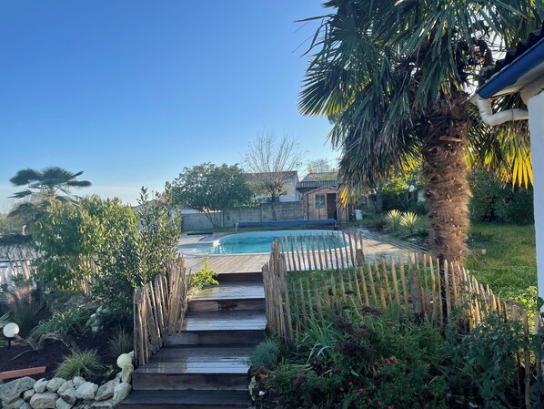 Ein Garten mit Swimmingpool, Holzstufen und verschiedenen Pflanzen und Bäumen.