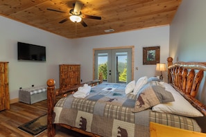 Een slaapkamer met een houten plafond, een bed met quilt, een televisie, een houten kledingkast, en een raam met uitzicht.