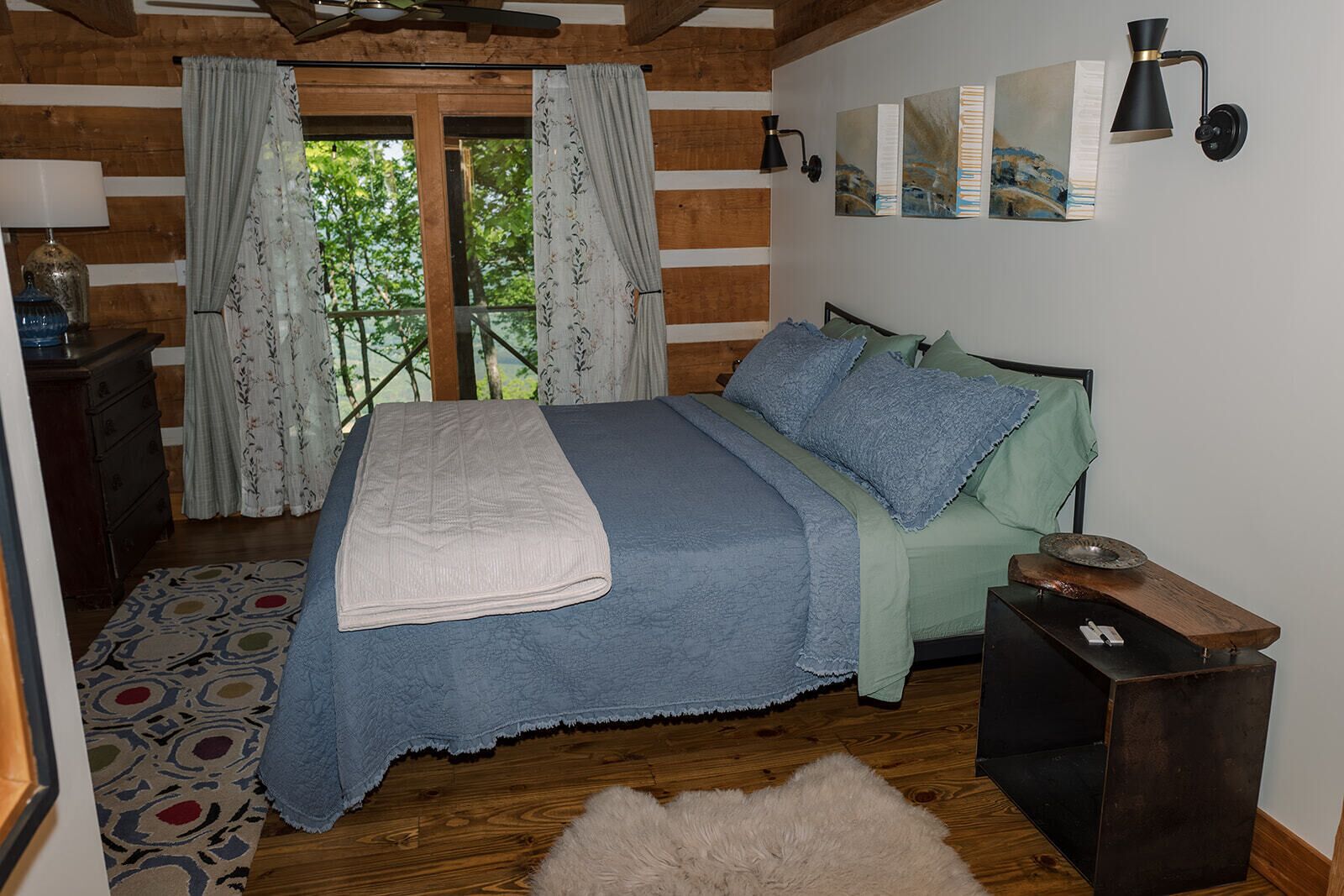 Una habitación con cama, mesita de noche, lámpara y ventana con cortinas.