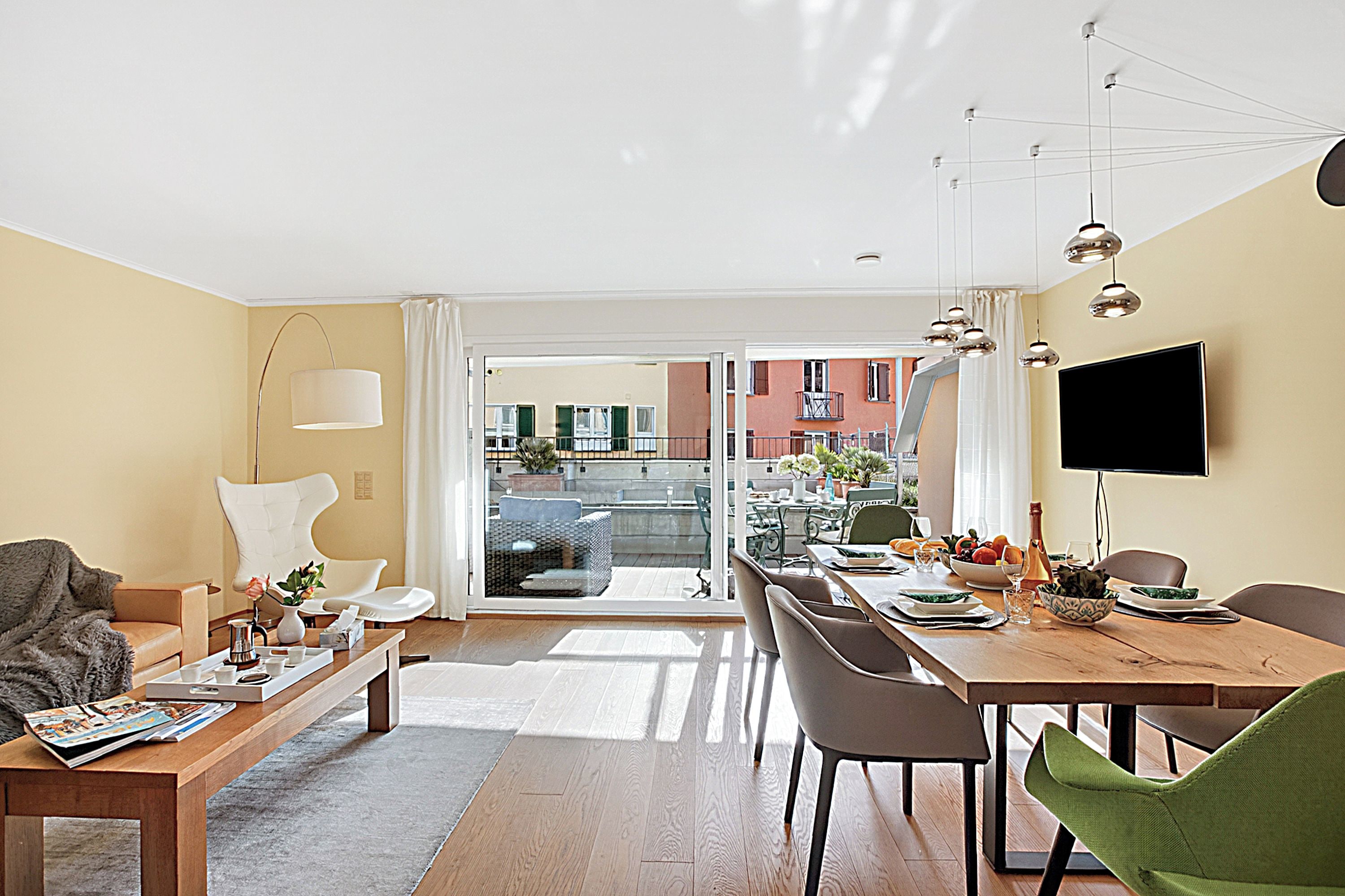 A modern living room with a sofa, coffee table, dining table, chairs, and a TV.