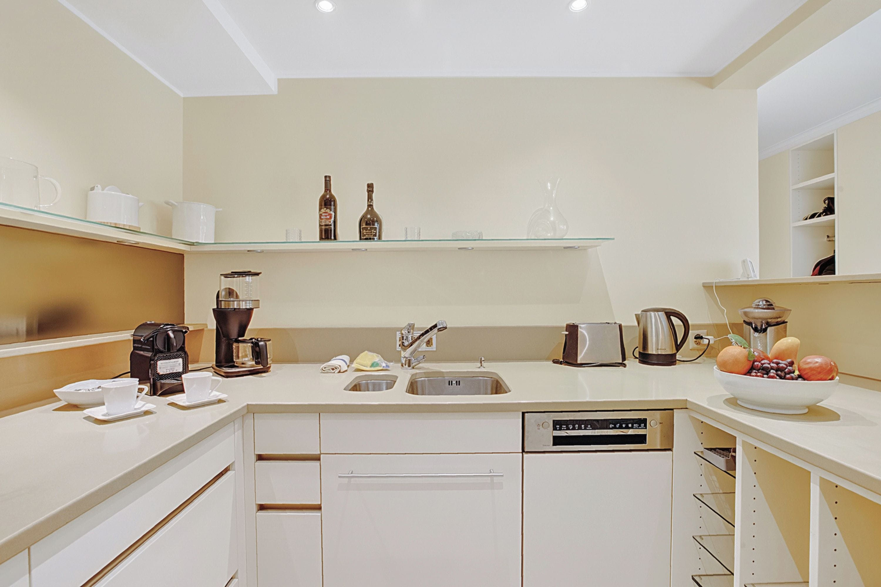 A modern kitchen with a dishwasher, coffee maker, and a fruit bowl on the counter.