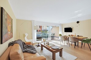 Ein modernes Wohnzimmer mit Sofa, Couchtisch und Essbereich mit Stühlen sowie einem Fernseher.