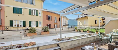 An outdoor patio with a wooden deck, outdoor furniture, potted plants, and a view of neighboring buildings.
