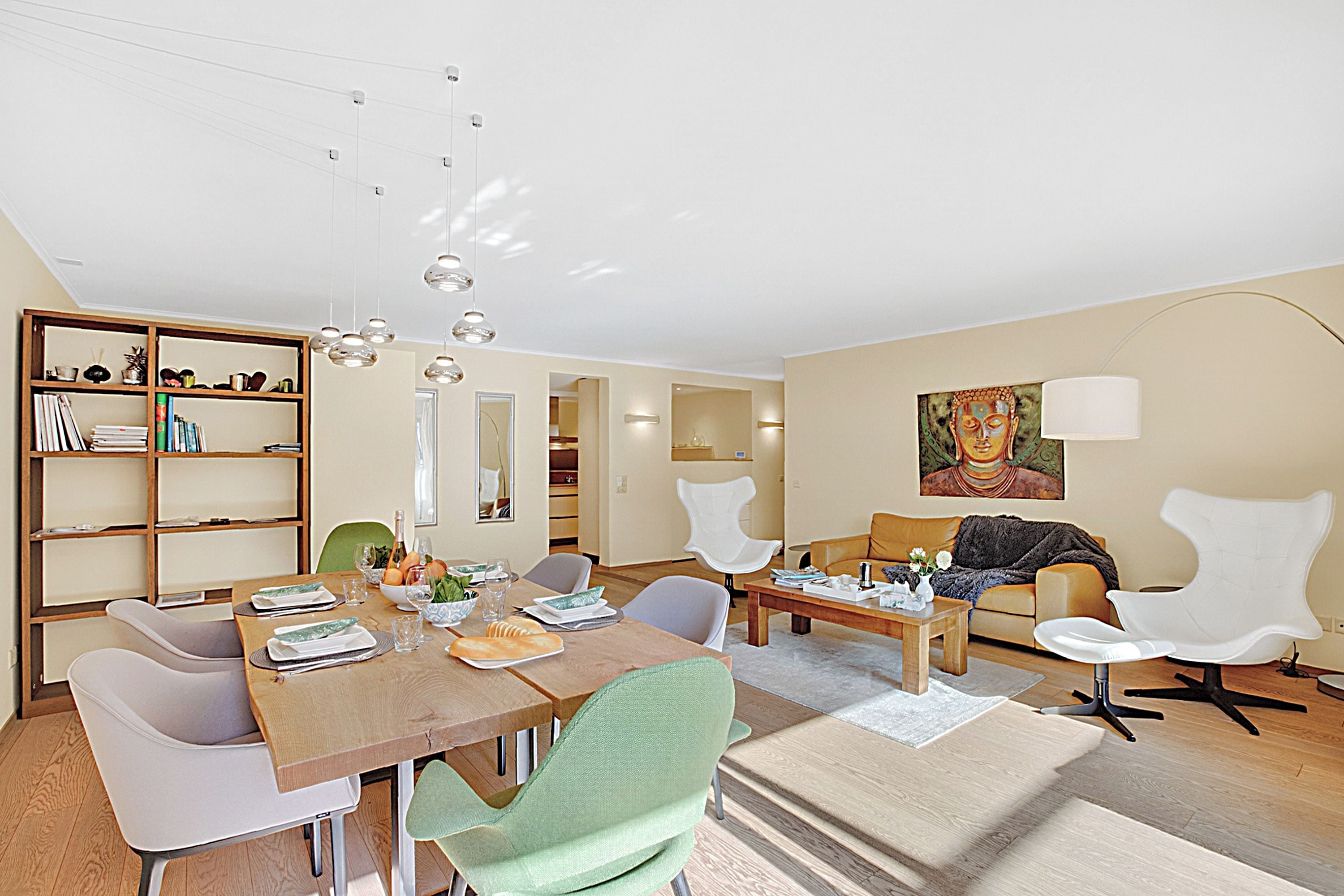 A modern living room with a dining area, a bookshelf, and a painting on the wall.