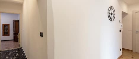 A hallway with a clock on the wall, a door at the end, and a marble floor.