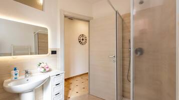 A bathroom with a white sink, a mirror, a clock, and a glass shower enclosure.