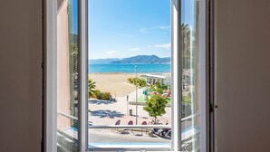 Vista desde una ventana de un lugar junto a la playa, con cielo despejado, arena y montañas a lo lejos.