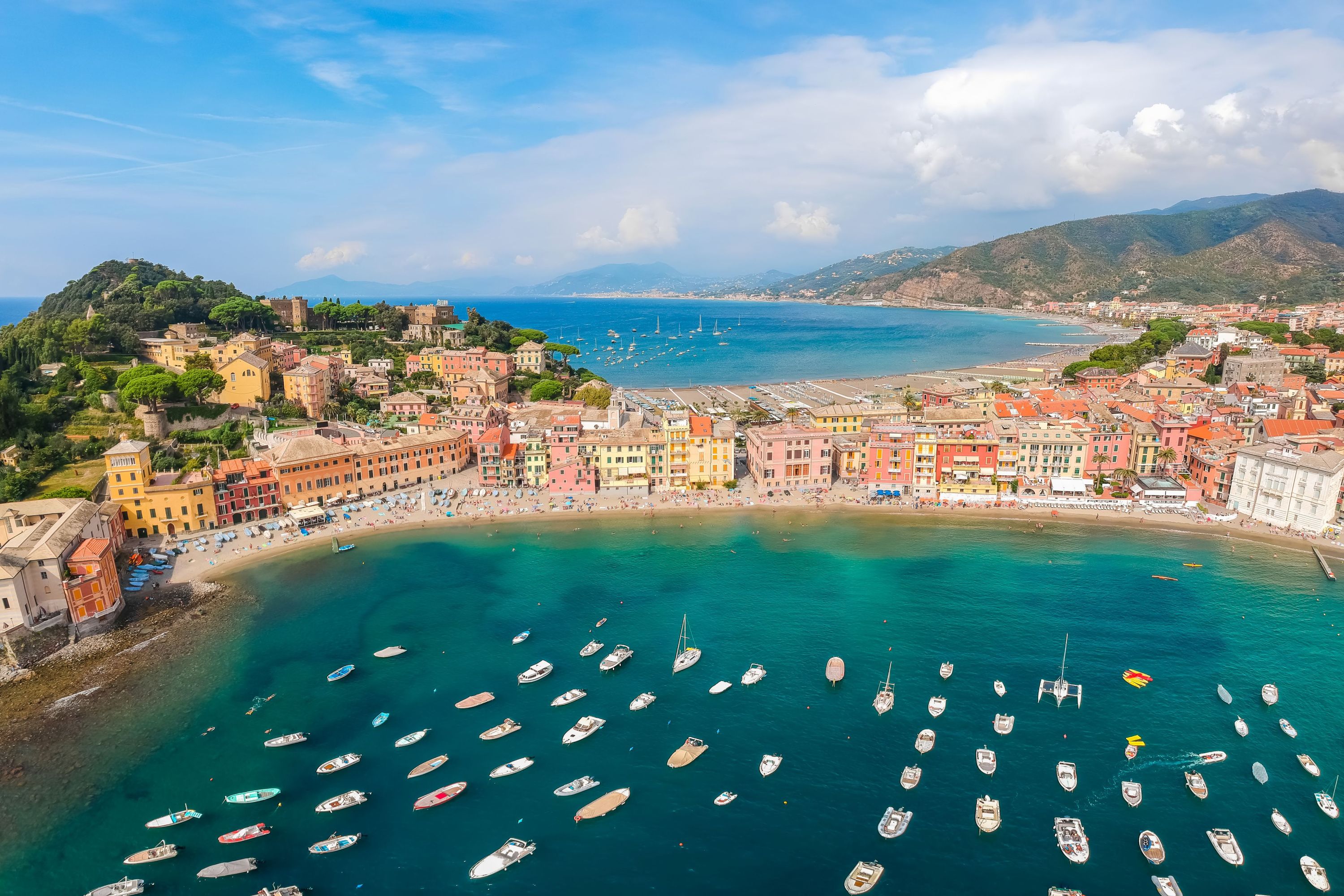 Una cittadina costiera con edifici colorati, un porto turistico con numerose imbarcazioni e una zona spiaggia.