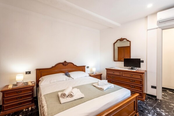 A hotel room with a wooden bed, bedside tables with lamps, a TV, a mirror, and a wardrobe. - Da Lino Beachfront Apartment for 4 (Sestri Levante)