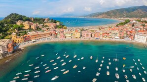 Un pueblo costero con edificios coloridos, un puerto deportivo con numerosos barcos y una zona de playa.