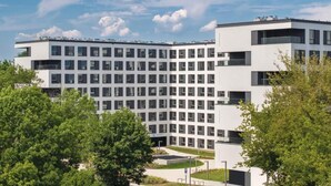 A modern multi-story building with a grid of windows, surrounded by greenery. - Zeitraum Raclawicka (Kraków)