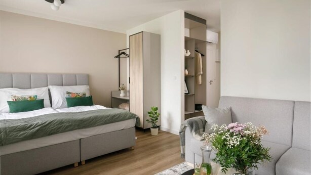A modern bedroom with a bed, bedside table, and a small seating area with a sofa and a coffee table. - Zeitraum Raclawicka (Kraków)