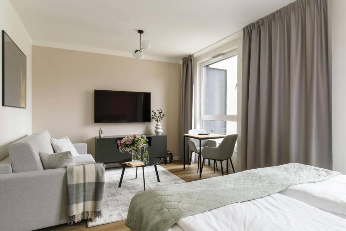 A modern hotel room with a bed, sofa, TV, desk, and window with curtains.