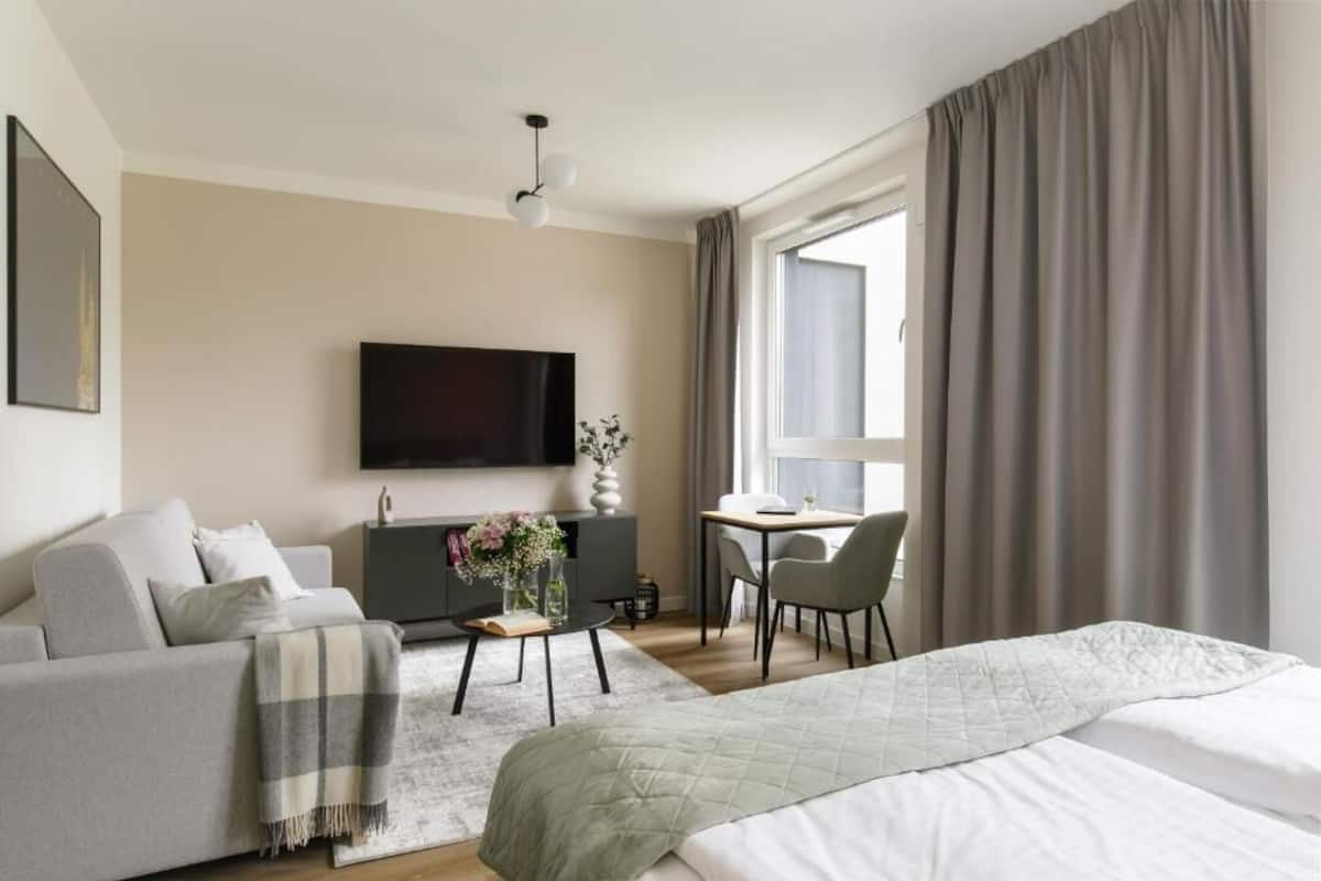 A modern hotel room with a bed, sofa, TV, desk, and window with curtains.