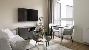 A modern living room with a sofa, a coffee table with a book, a TV, a dining area with chairs, and a large window. - Zeitraum Raclawicka (Kraków)