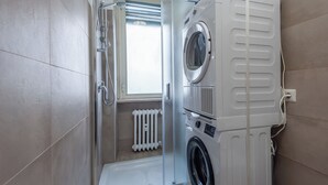 Een kleine wasruimte met een wasmachine, droger en een klein raam.