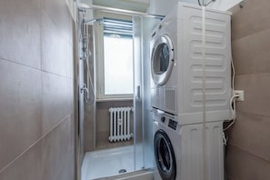 A compact laundry room with a washing machine, dryer, and a small window. - Bright & Stylish Flat near Villa Pamphili (Roma)