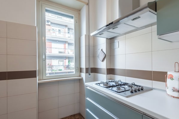 A kitchen with a gas stove, a window with a view of a balcony, and a tiled backsplash. - Bright & Stylish Flat near Villa Pamphili (Roma)