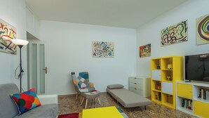 Een moderne woonkamer met een bank, een fauteuil, een kleine tafel, een televisie en een boekenkast.